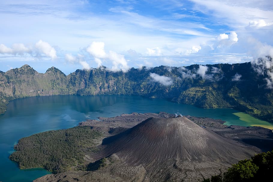brown and green mountain surrounded by calm water at daytime, bird's eye photography of volcano neat water HD wallpaper