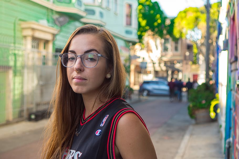 women's red and black basketball jersey standing on road, selective focus photography of woman wearing eyeglasses and NBA jersey