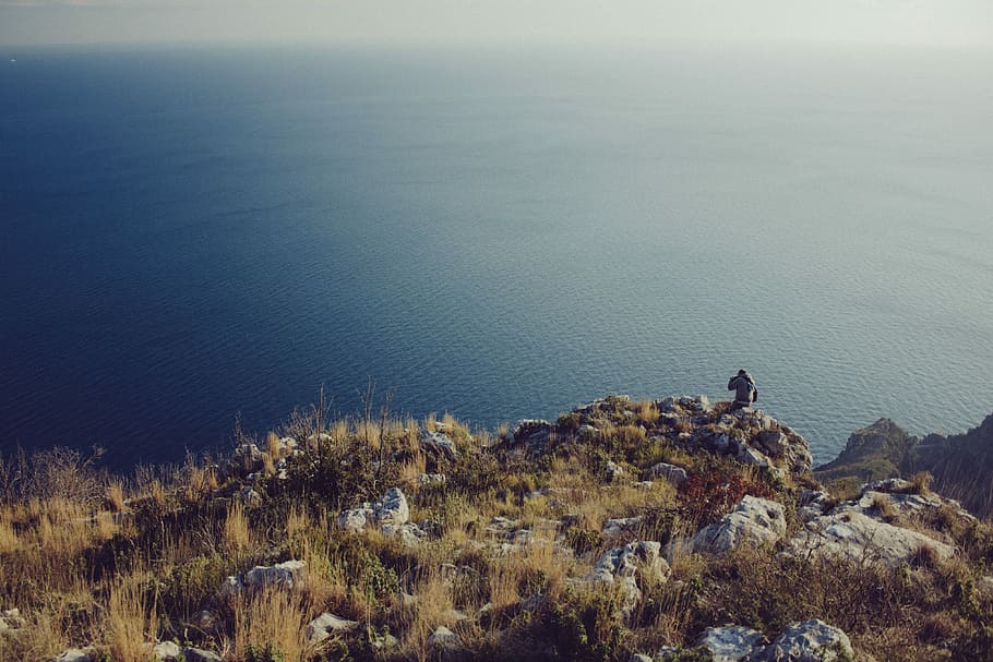 person  standing near cliff with viewing body of water during cloudy day HD wallpaper