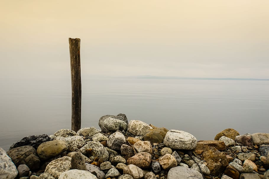 stones and brown wooden stick near body of water under cloudy sky, brown stone stacked together, HD wallpaper