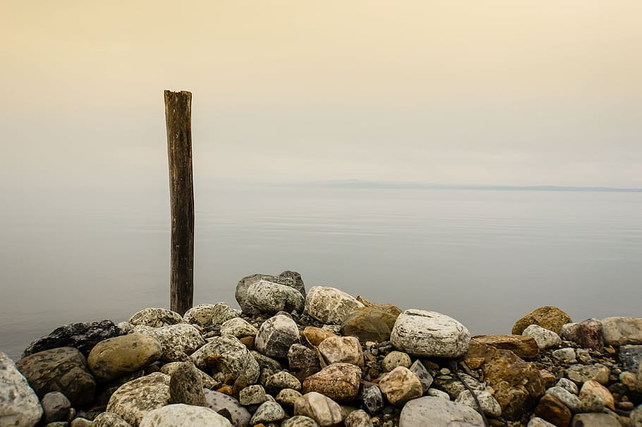 stones and brown wooden stick near body of water under cloudy sky, brown stone stacked together HD wallpaper