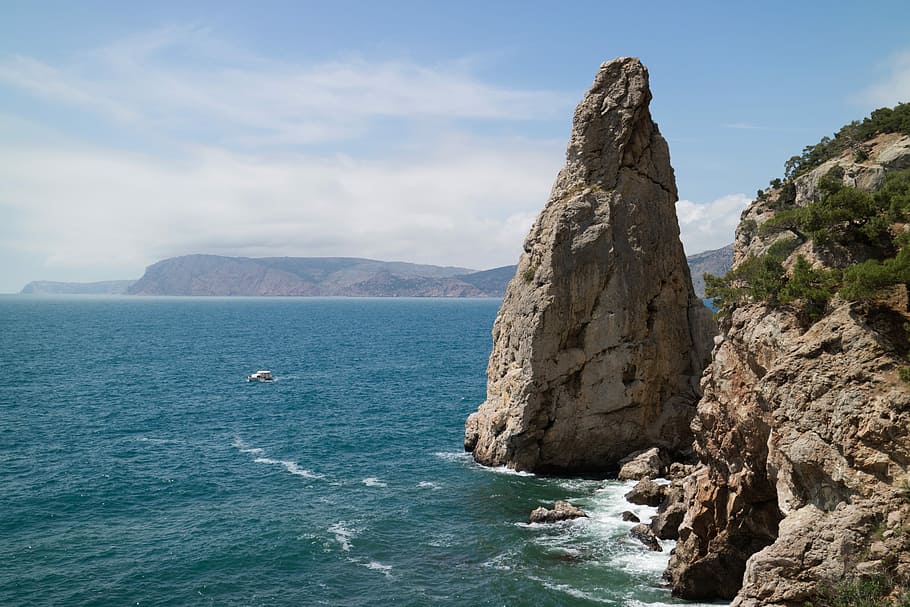 photo of island and horizon, brown rock monolith on body of water