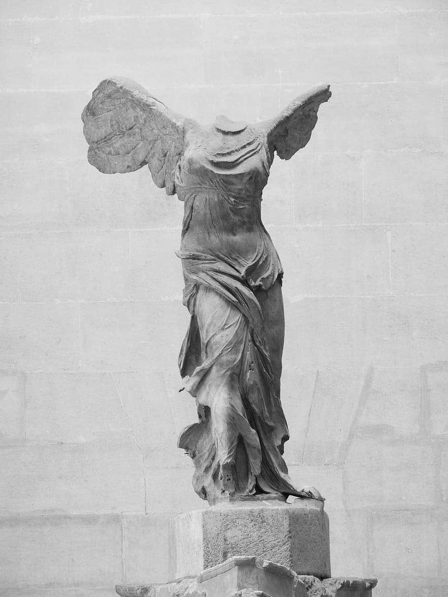 concrete angel statue with broken head beside gray concrete wall