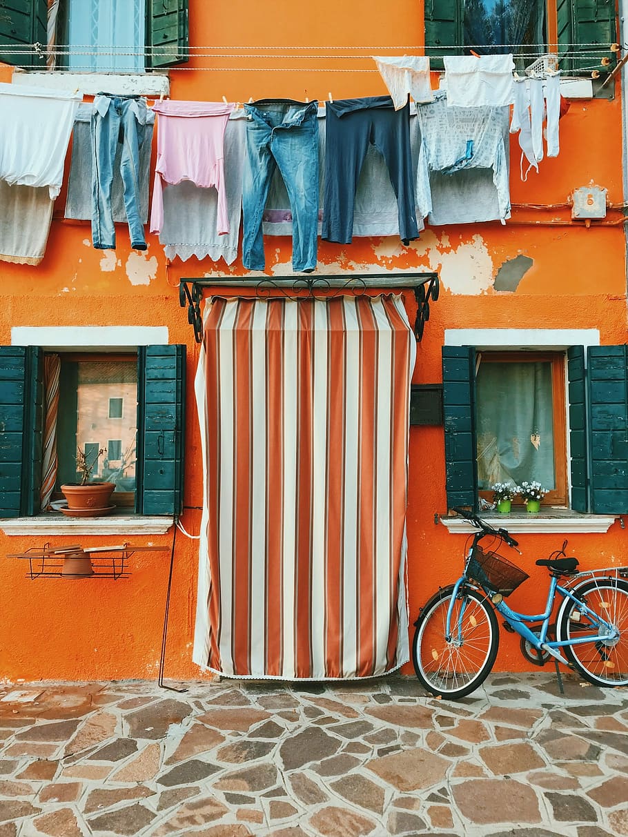 red and white cover beside blue bike, clothes hanged in front of orange building above blue bicycle parked near pathway, HD wallpaper