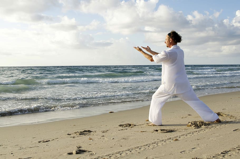 Man dressed in White Practicing Tai-Chi on the Beach, clouds