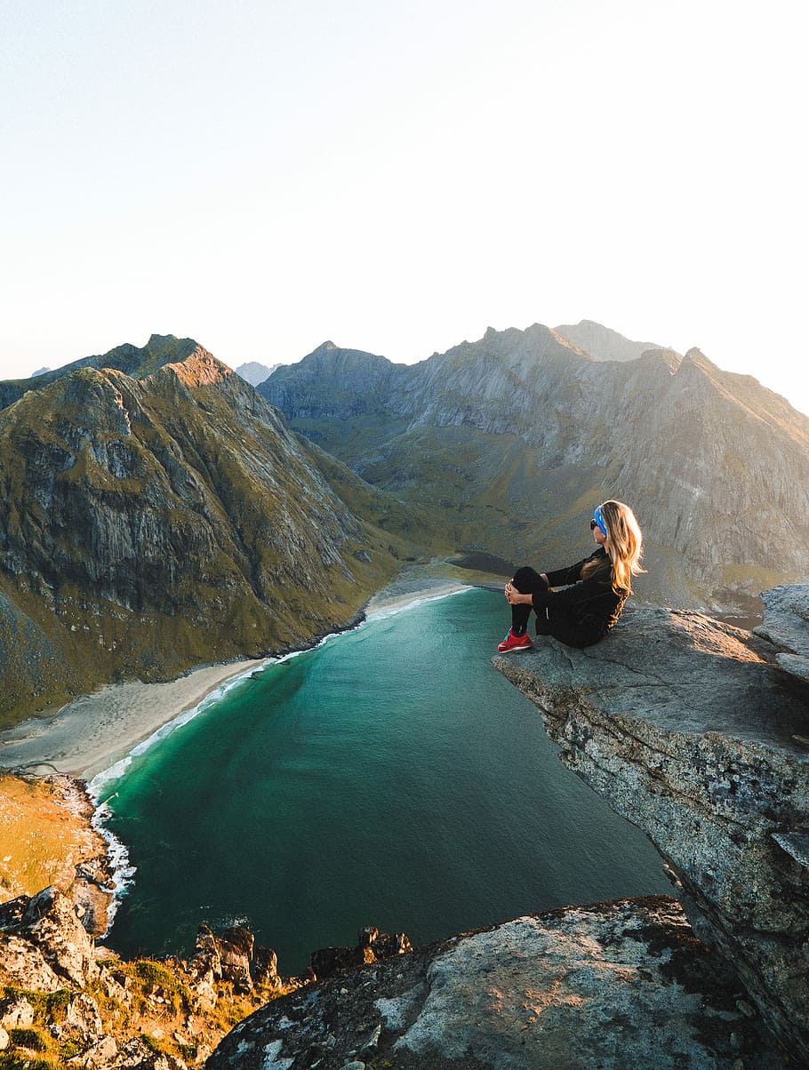 woman sitting on cliff overlooking body of water near mountains during daytime, woman sitting beside cliff HD wallpaper