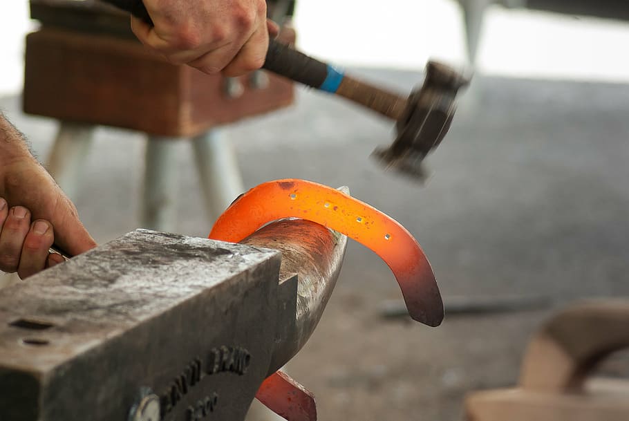 person holding glowing metal on anvil, blacksmith, hammer, farrier