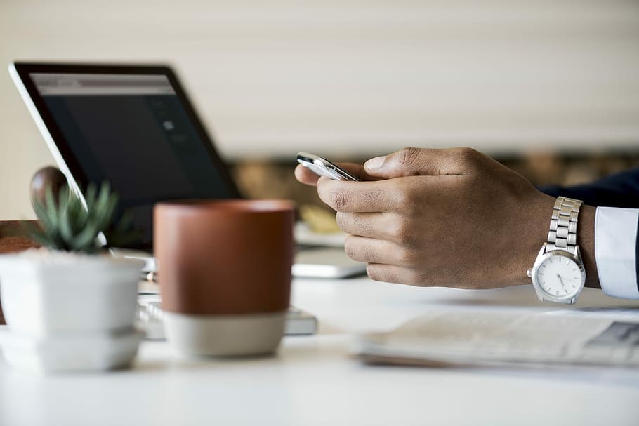 person wearing round white analog watch while holding smartphone in front of turned-on laptop computer, HD wallpaper