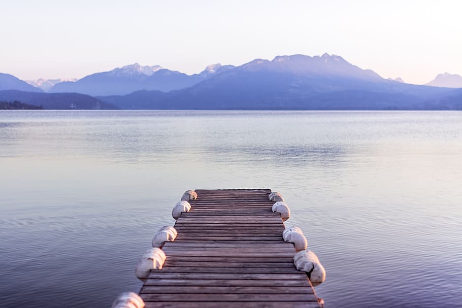 brown wooden boat dock in gray skies background, brown wooden dock and body of water near mountains under clear blue sky photo taken during daytime