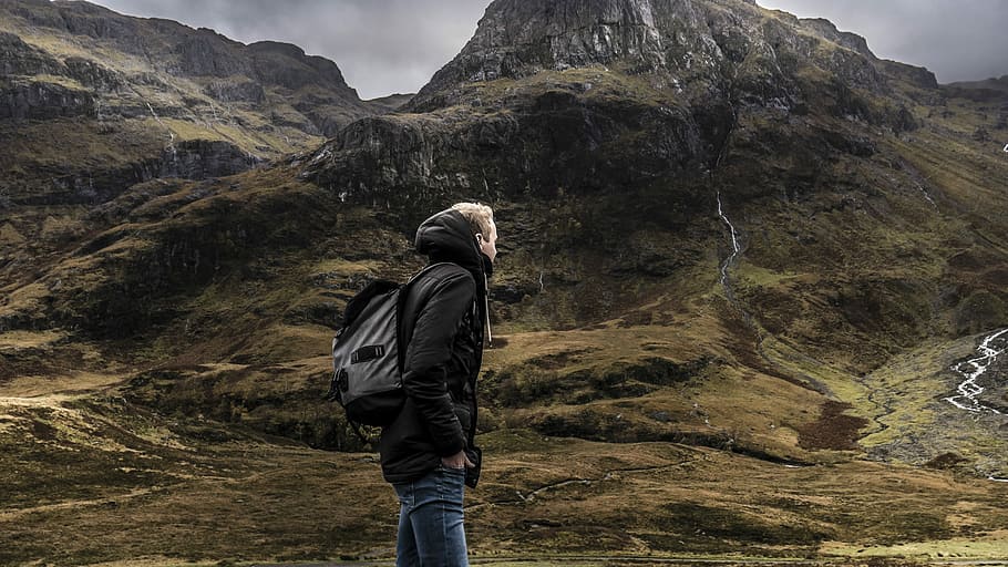 man standing in front mountain under gray sky, man standing on mountain with mountain range background HD wallpaper