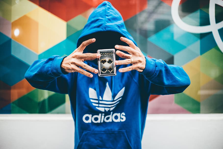 person wearing blue adidas pullover hoodie levitating playing card