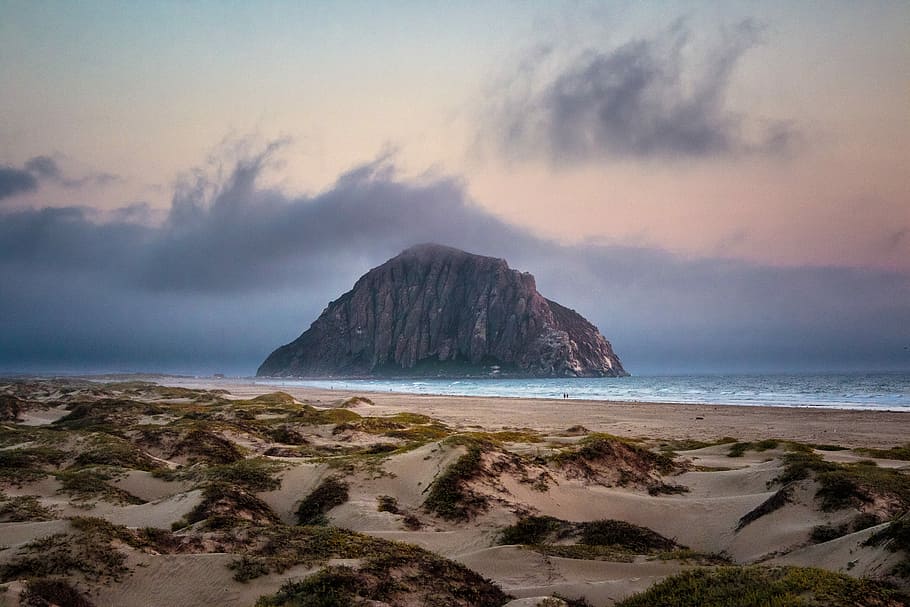 landscape photo of brown mountain surrounded by body of water near seashore, stack landform at cloudy sky HD wallpaper