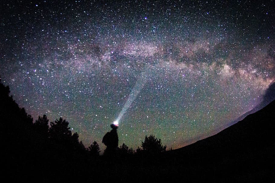silhouette of person pointing flashlight on starry sky during nighttime HD wallpaper