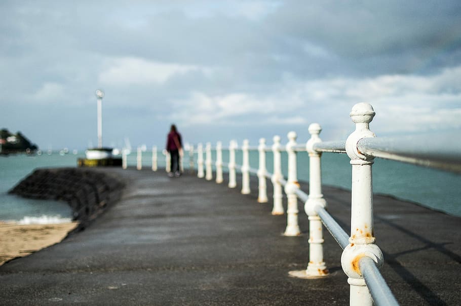 shallow focus photography of man near shore during daytime, person walking on black path near sea shore HD wallpaper