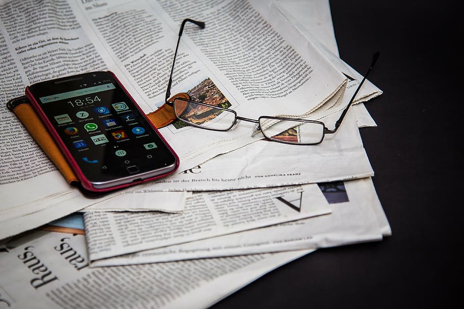 black Motorola Android smartphone and brown flip case, newspaper