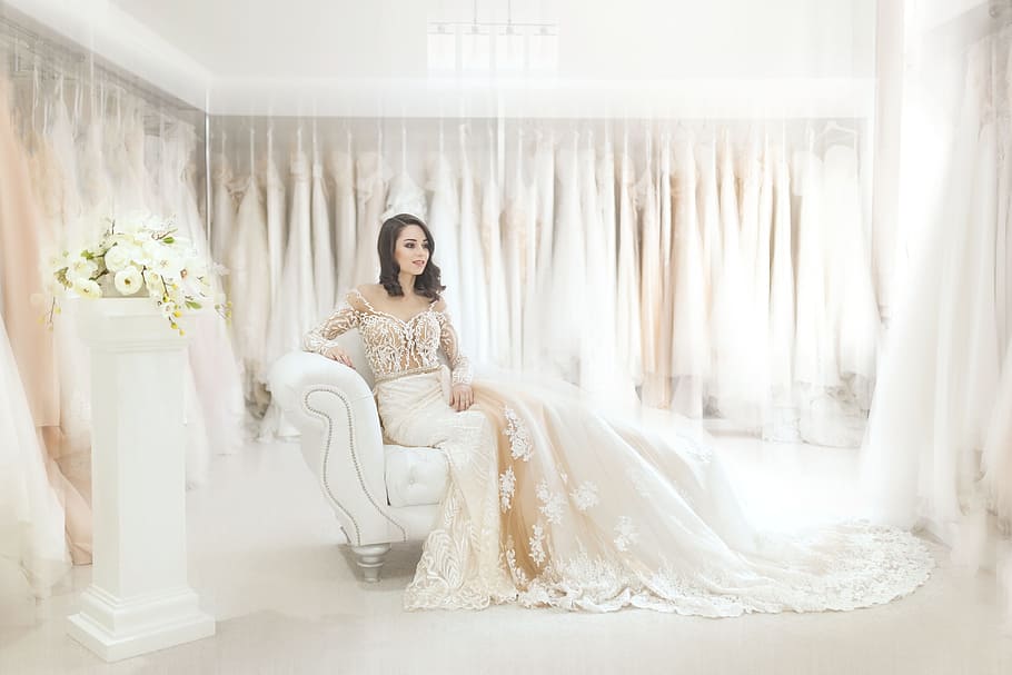 woman sitting on white leather armchair inside house, woman in white wedding dress seating on couch