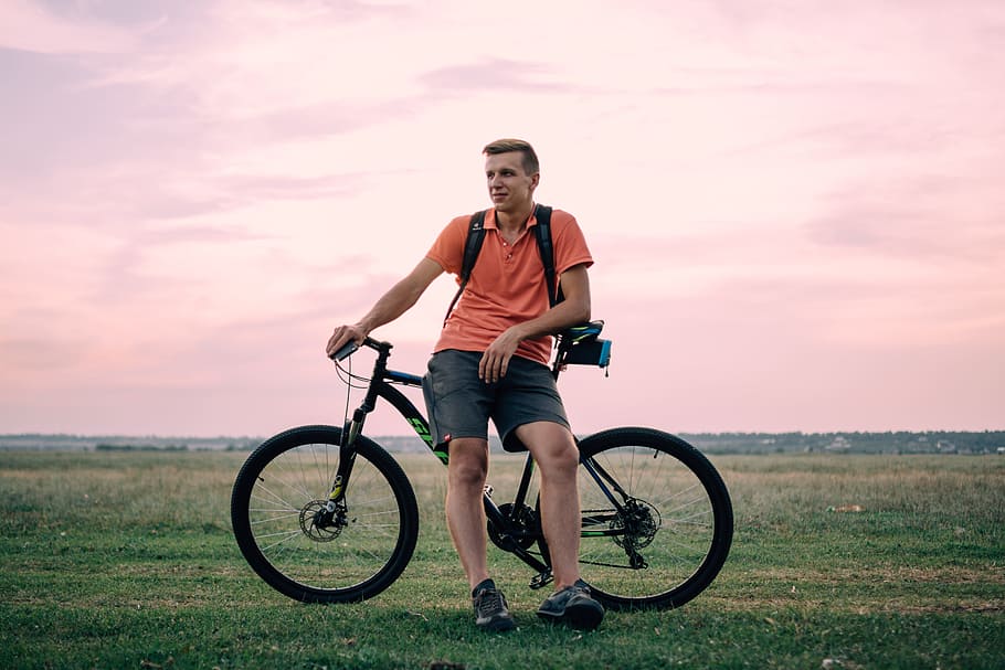 man sitting on hardtail bike under golden hour, man leaning on black bicycle on open field