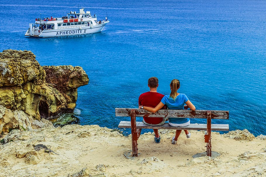 boy and girl seat on brown bench facing on ocean and boat during daytime, HD wallpaper