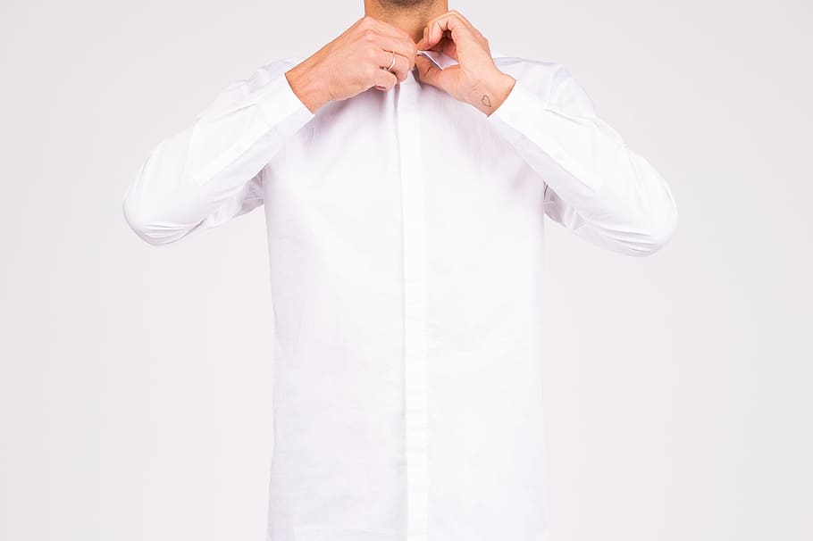 A man buttoning up a white shirt, person's holding white collar dress shirt