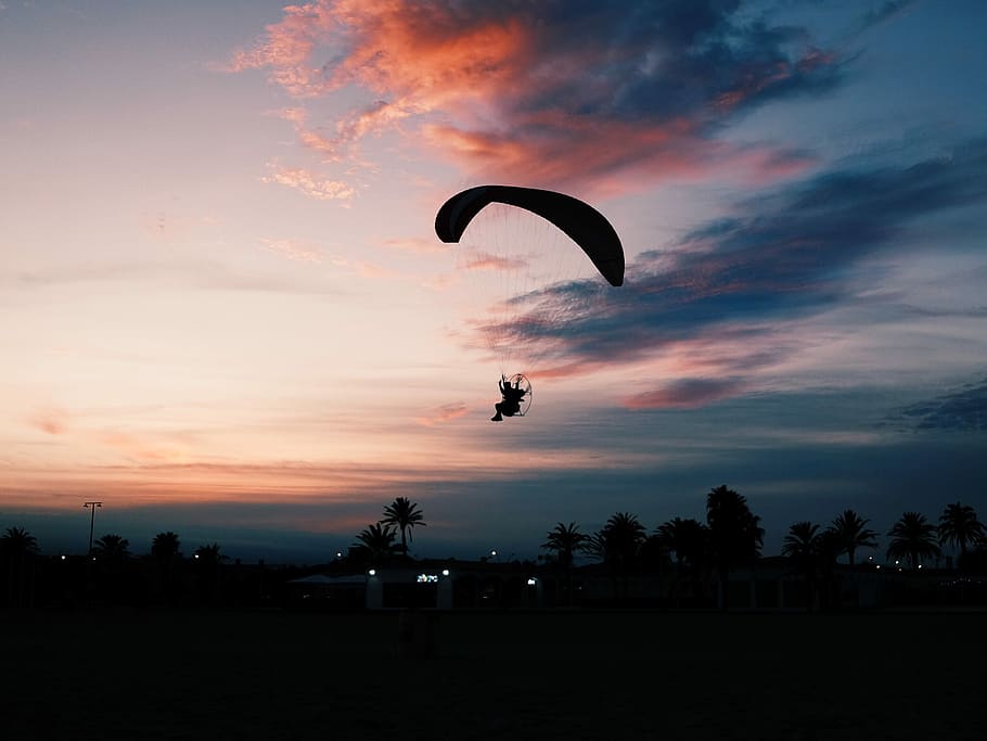 silhouette of man parachuting under gray sky, silhouette photo of man skydiving landing on land at noontime