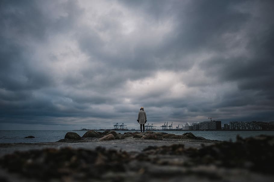person standing on sea shore under dark clouds, person standing on dock HD wallpaper