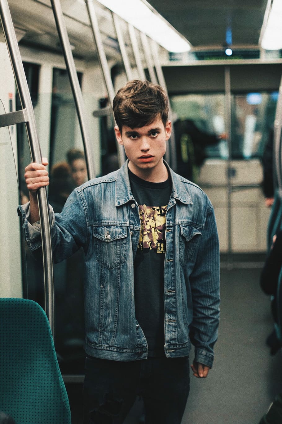 man wearing blue denim jacket standing inside train, man standing inside train while holding bar