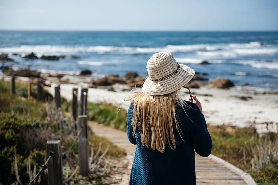 woman walking on seashore, woman wearing brown hat standing on beach HD wallpaper