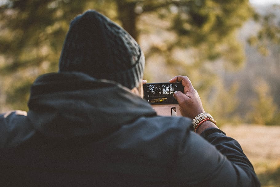 person taking photo using smartphone, man in black hoodie holding black camera HD wallpaper