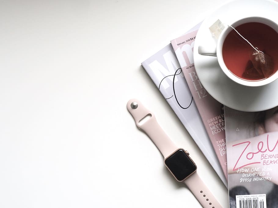 rose gold aluminum case Apple Watch with pink Sport Band beside white ceramic teacup filled with red liquid placed on white wooden board