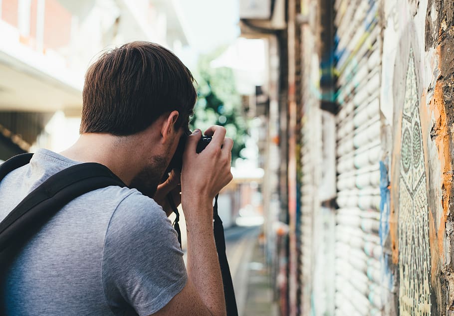 man taking a photo of wall painting during daytime, shallow focus photography of man holding camera during daytime HD wallpaper