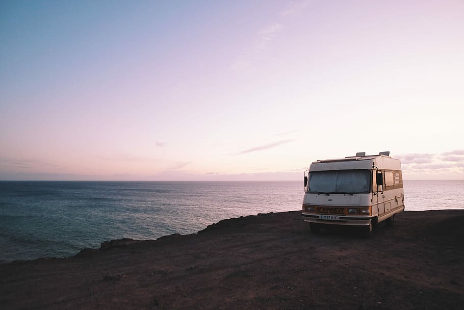 RV parked beside the edge of island during sunset, white vehicle parked on cliff HD wallpaper