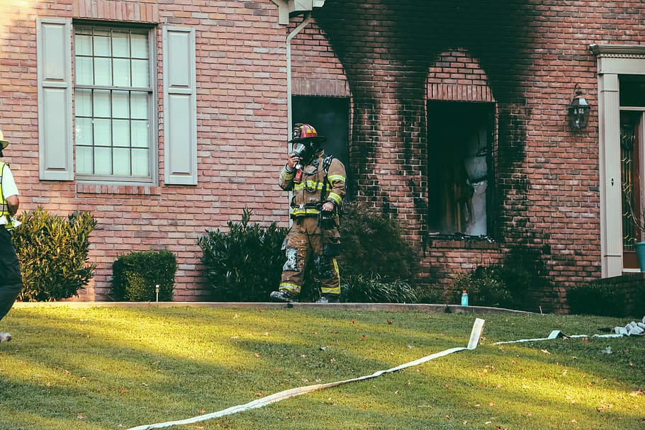 fireman walking in front of brown brick house, fireman walking in yard outside brown brick house at daytime HD wallpaper