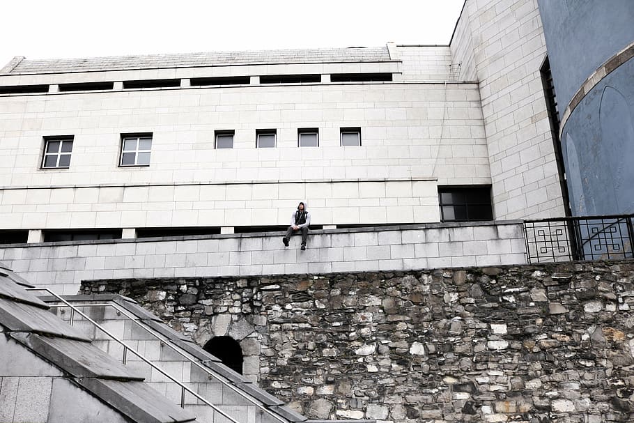 man sitting on white concrete building, grayscale, photography HD wallpaper