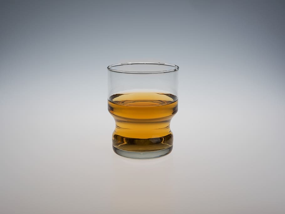 clear drinking glass filled with yellow liquid, liquor, isolated