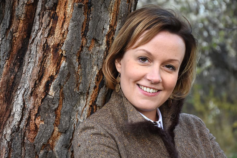woman wearing brown collared jacket leaning on tree trunk, autumn