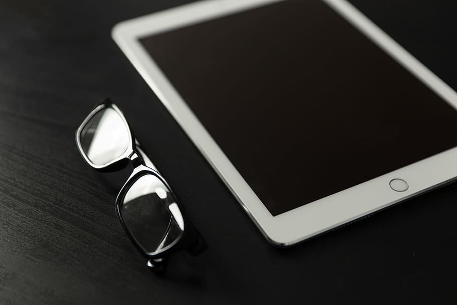 The new 9.7″ iPad Pro tablet with reading glasses on a black desk