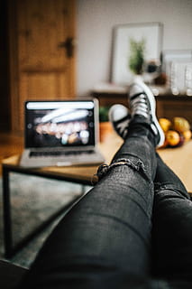 Woman in ripped jeans and black sneakers with a silver laptop on a wooden table HD wallpaper