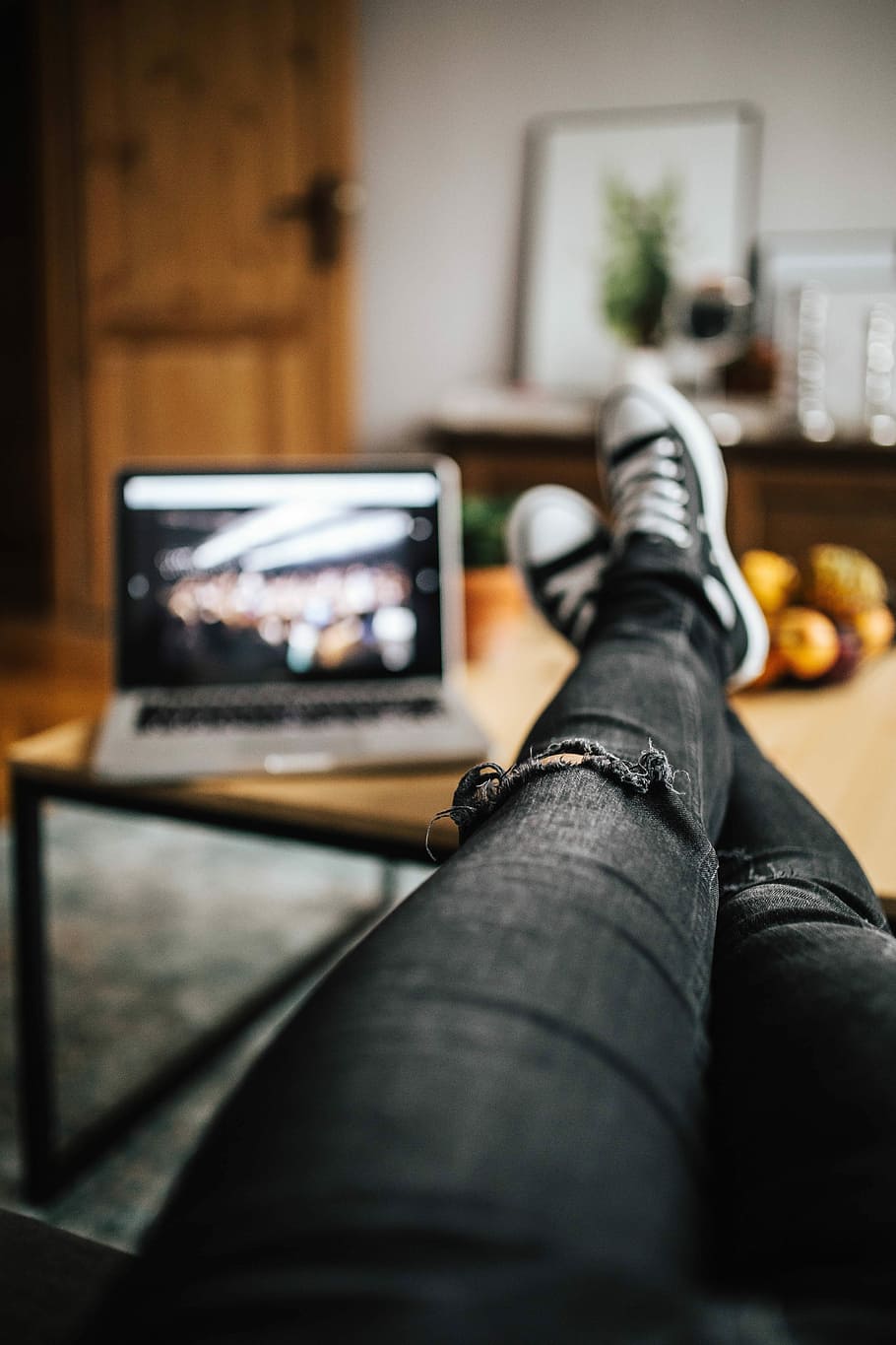 Woman in ripped jeans and black sneakers with a silver laptop on a wooden table HD wallpaper
