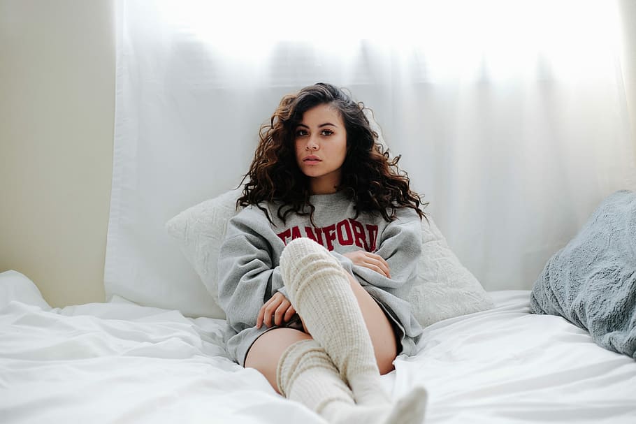 woman lying on bed, woman in gray sweatshirt sitting on white textile HD wallpaper