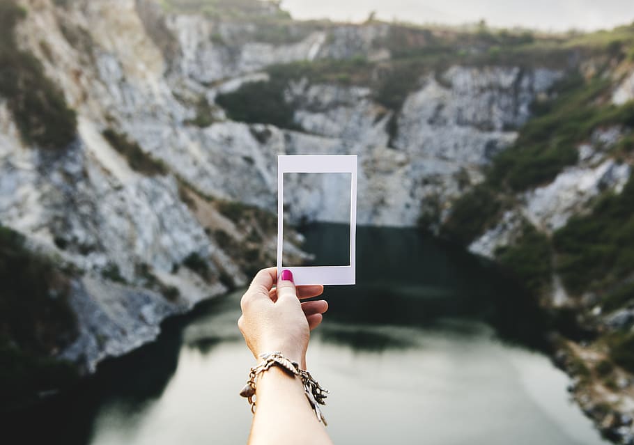 woman wearing silver-colored bracelet holding insta film near mountain during daytrime HD wallpaper