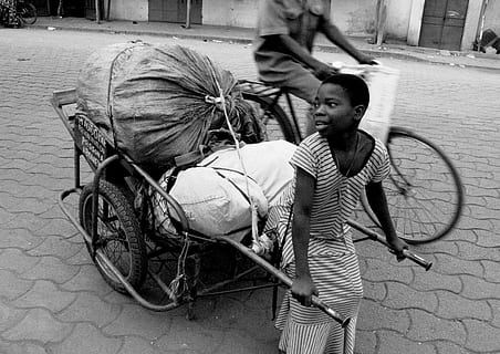 grayscale photo of boy pulling cart near man riding on bicycle during daytime HD wallpaper