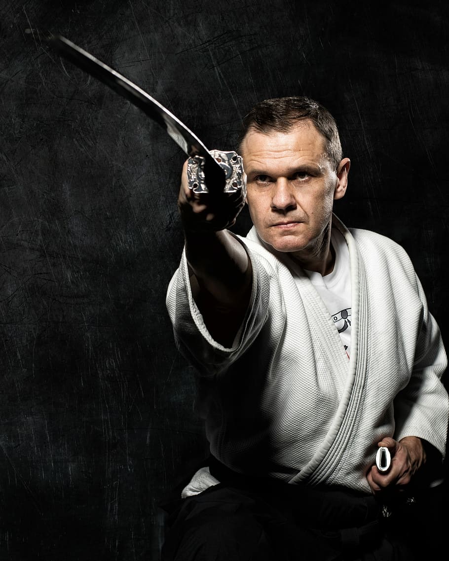 Photosession with katana, man wearing white karate gi holding sword