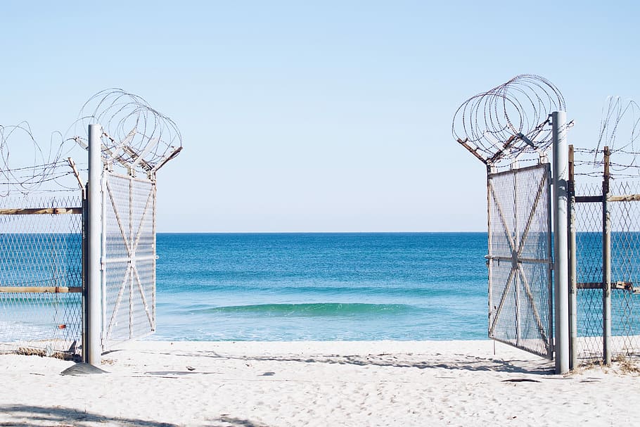 photography of white opened gate with barb wire, cyclone fences on beach
