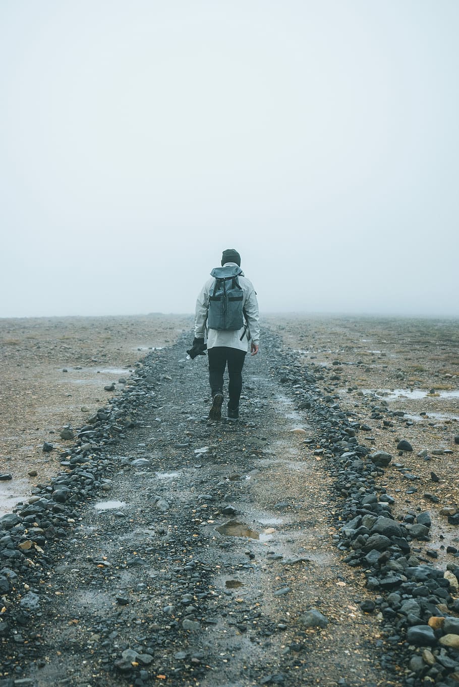 man with backpack walking on brown field, man walking on gray sand HD wallpaper