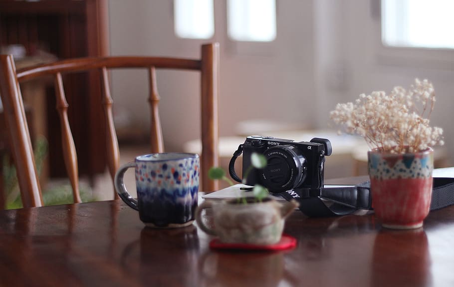 black camera on table, selective focus photograph of DSLR camera near mug and pot on wooden table, HD wallpaper