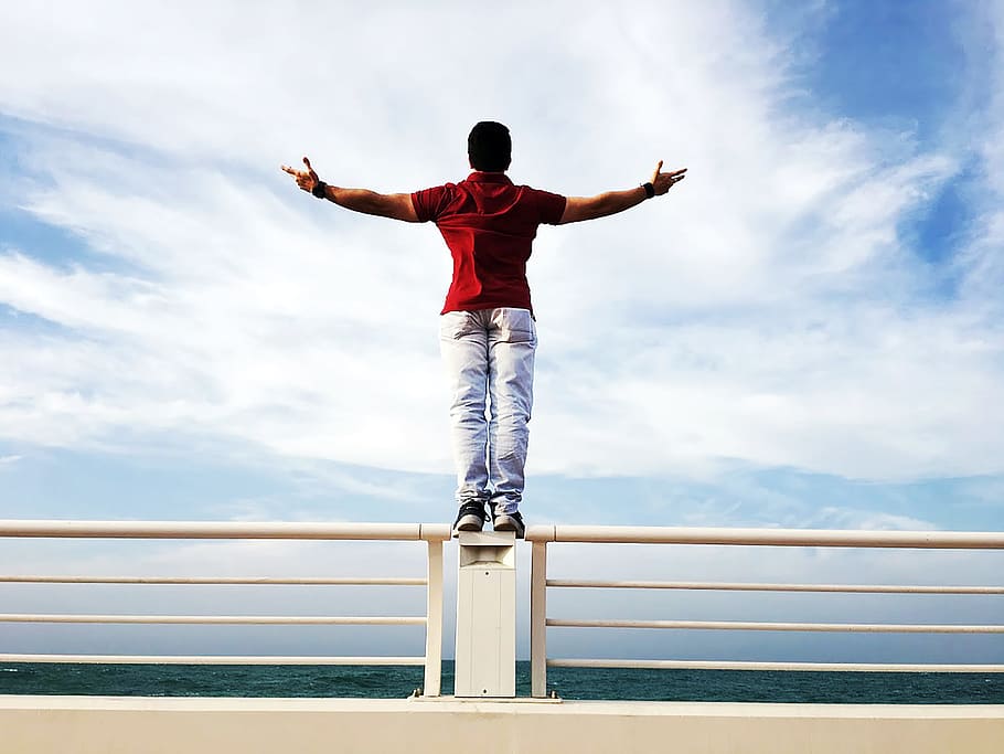 Person Raising Hands Mid-air Sidewards While Standing on Gray Steel Railings HD wallpaper