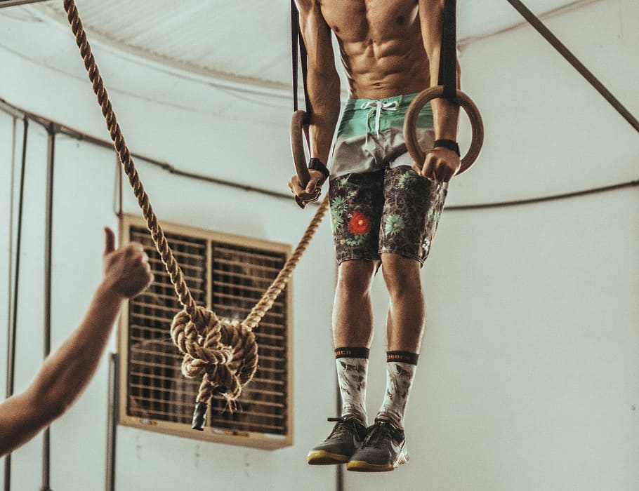man wearing multicolored shorts while exercising on rope inside white room, man holding on rings HD wallpaper