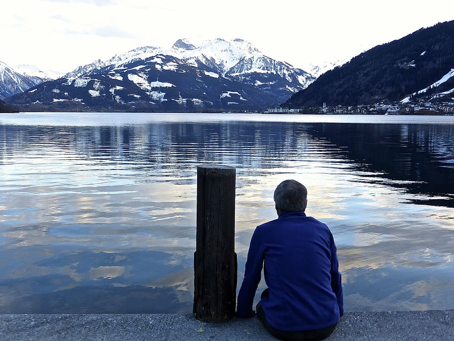 man sitting beside bollard facing body of water, lake, reflection
