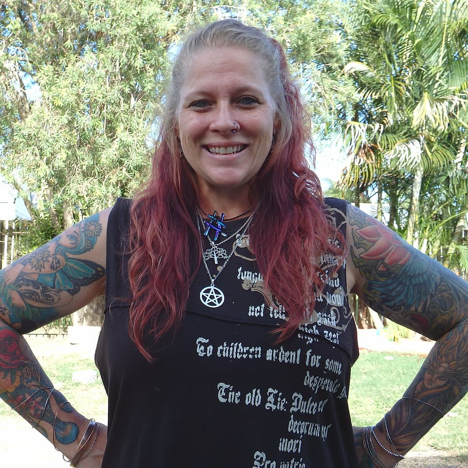 woman standing on grass field with hands on waist, tattooed, smile