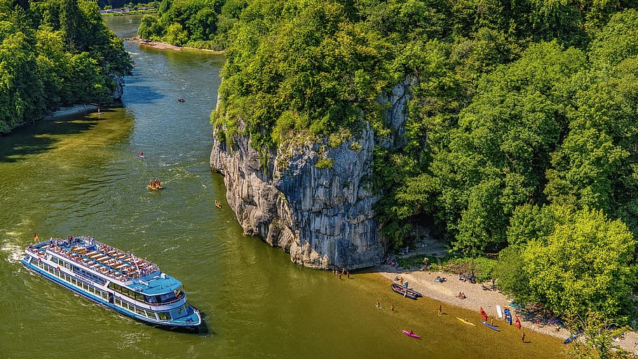 blue and white ship on body of water near gray rock formation during daytime HD wallpaper